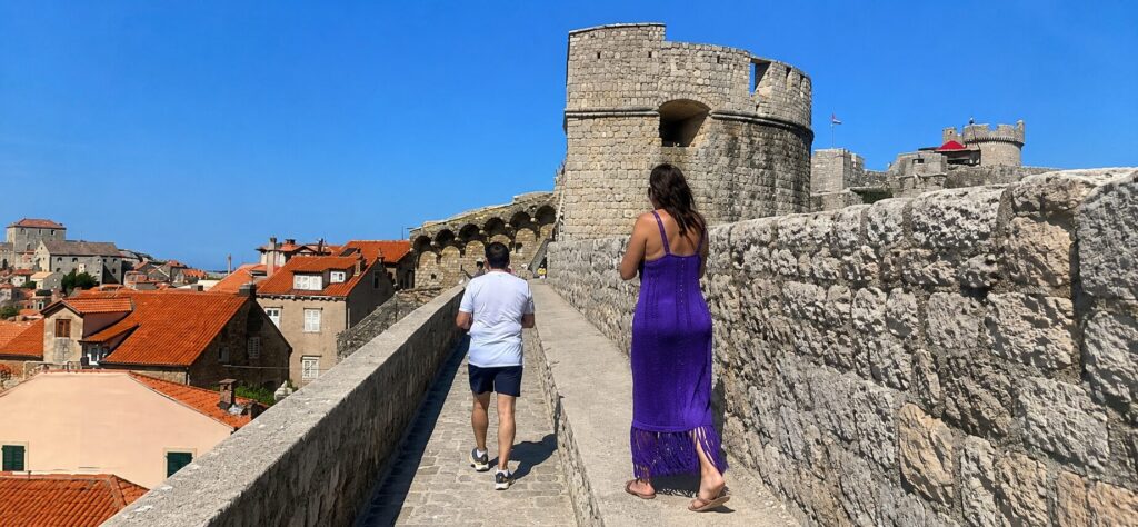 Visitors walking along the historic Dubrovnik City Walls overlooking Old Town rooftops on a sunny day