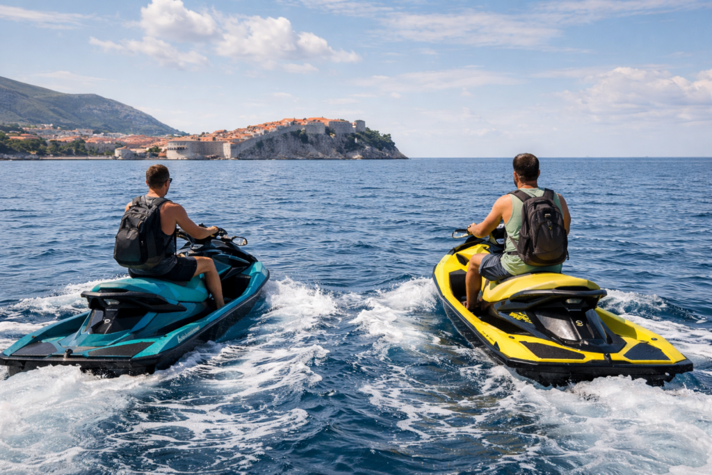 Two riders on jet skis approaching Dubrovnik Old Town across the Adriatic Sea.