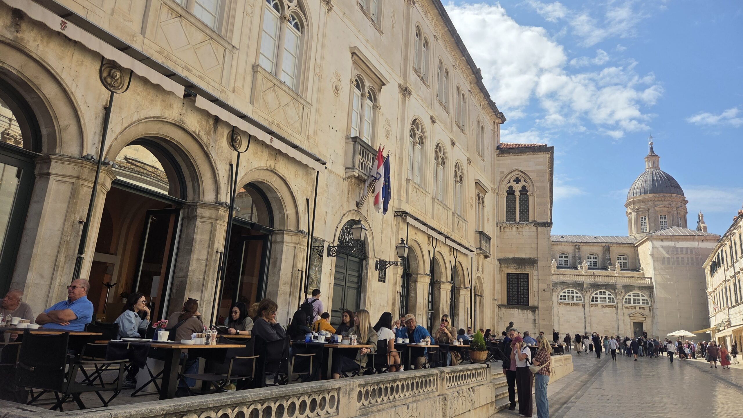 People enjoying coffee culture outside a café in Dubrovnik Old Town near the Cathedral on a sunny day