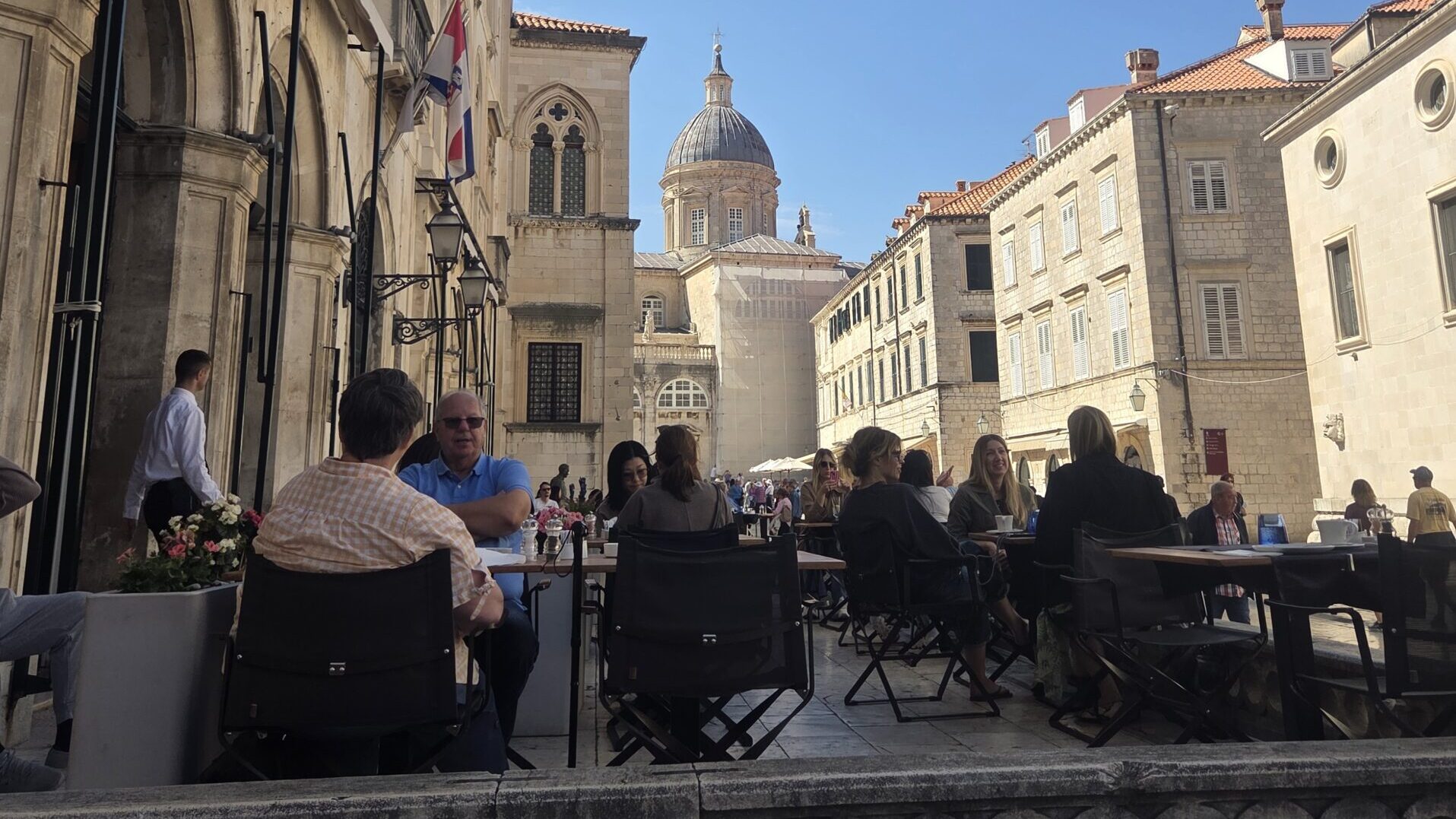 People enjoying coffee at an outdoor café in Dubrovnik Old Town with historic stone streets and Dubrovnik Cathedral in the background