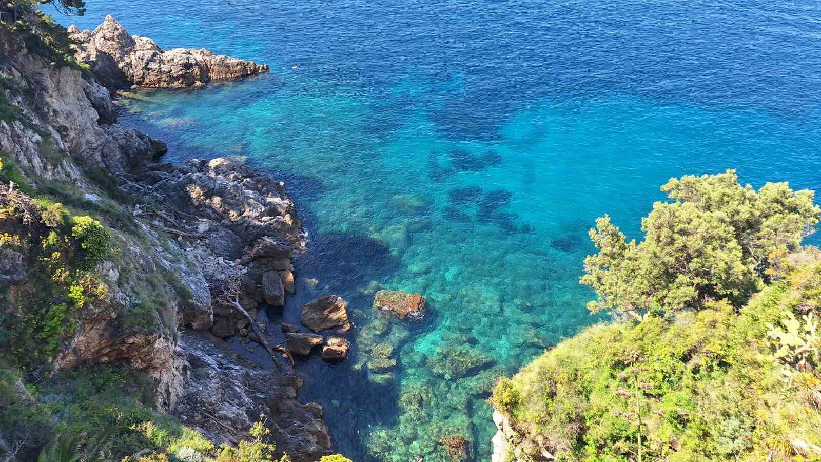 Crystal-clear Adriatic Sea near Dubrovnik with turquoise water, rocky coastline, and a sailboat anchored offshore.