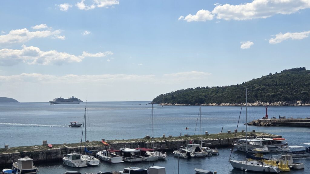 Cruise ship anchored near Dubrovnik with Lokrum Island and small boats visible from the Old Town harbor.