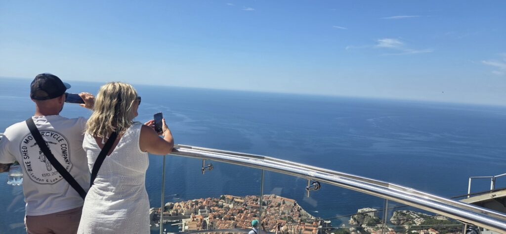 Cruise guests taking photos from a panoramic viewpoint above Dubrovnik Old City and the Adriatic Sea.