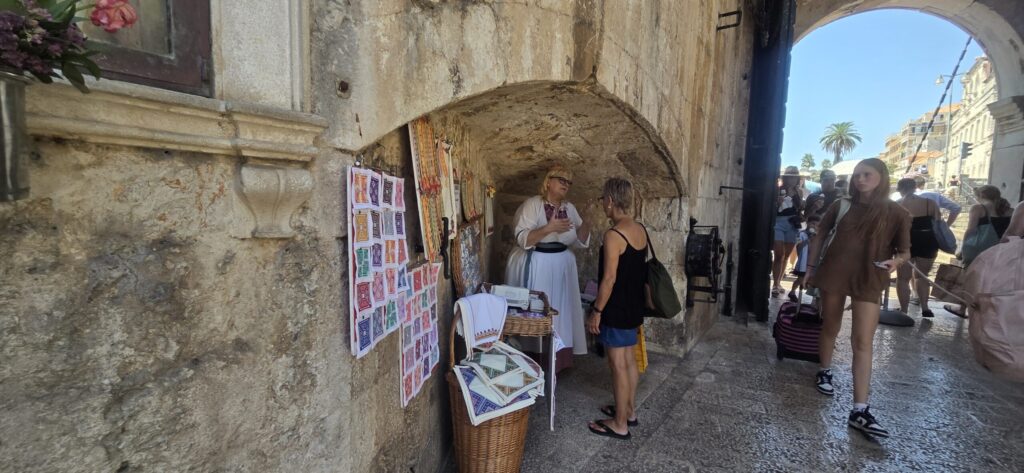 Ankica showing handmade souvenirs, embroidered tablecloths and traditional Konavle embroidery near Pile Gate in Dubrovnik Old Town.