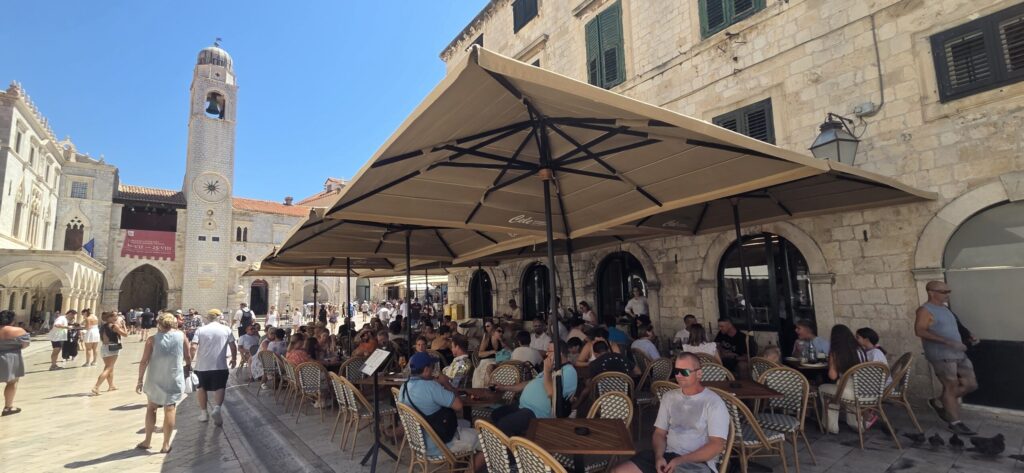 Cele café terrace on Stradun in Dubrovnik, with the Bell Tower and Luža Square visible in the background.