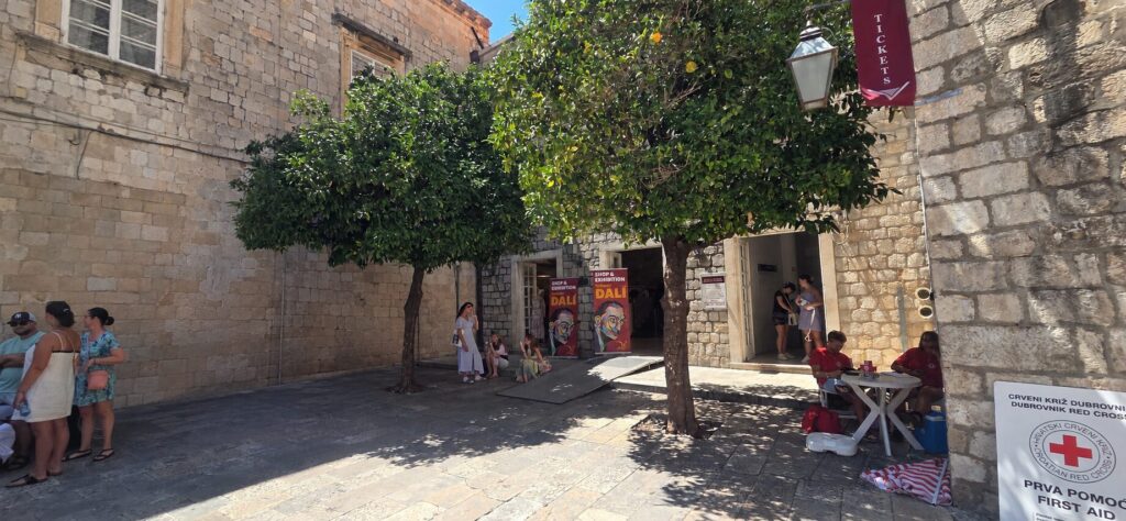 Salvador Dalí shop and exhibition near Stradun in Dubrovnik Old Town, set beneath orange trees beside the historic stone walls.